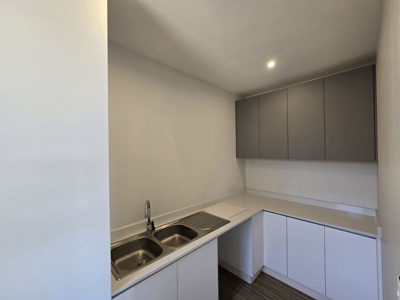 A clean and modern scullery featuring stone countertops, double stainless steel sink, and ample upper and lower cabinetry for organized storage.