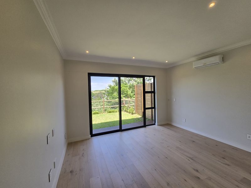 Bright and modern living room featuring timber flooring, recessed lighting, split-system air conditioning, and large sliding doors opening to a private garden area.
