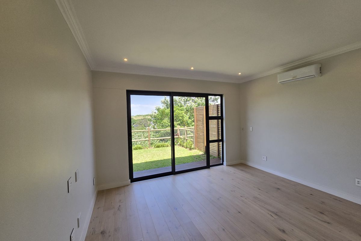 Bright and modern living room featuring timber flooring, recessed lighting, split-system air conditioning, and large sliding doors opening to a private garden area.