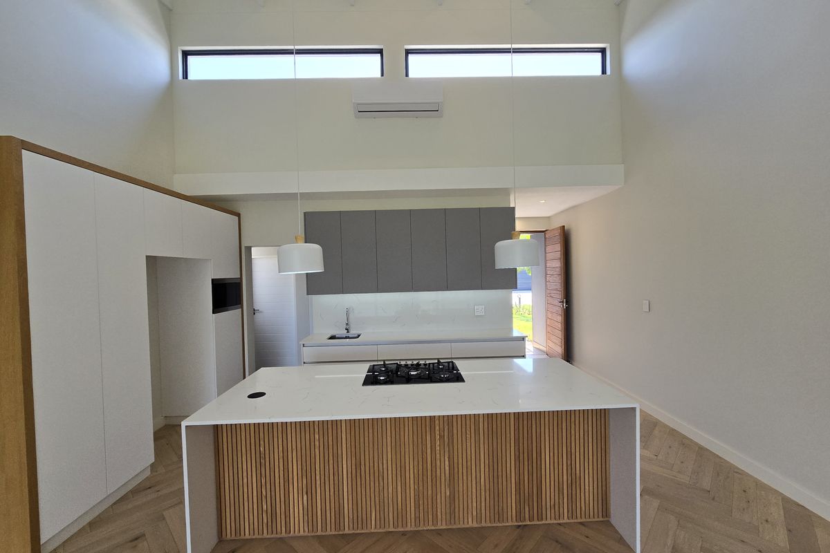 Modern kitchen featuring a central island with gas cooktop, stone countertops, herringbone timber flooring, and high ceilings with clerestory windows for natural light.