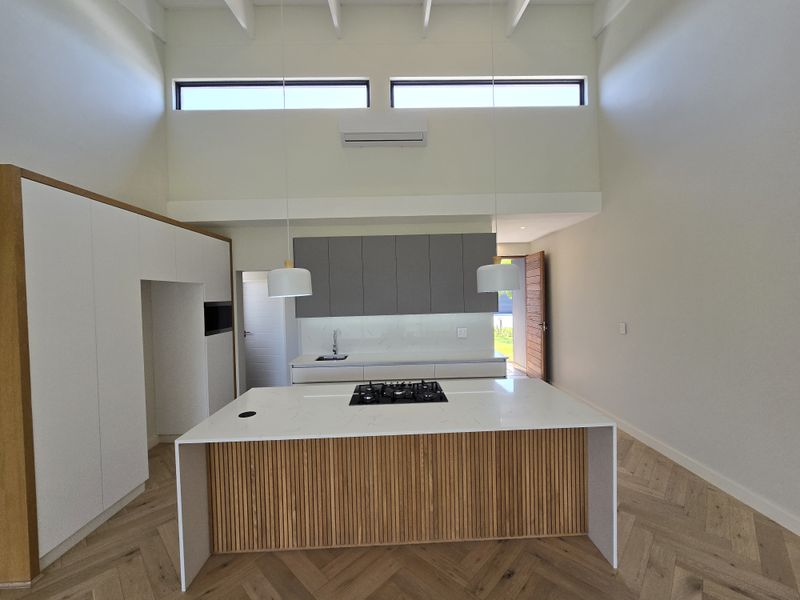 Modern kitchen featuring a central island with gas cooktop, stone countertops, herringbone timber flooring, and high ceilings with clerestory windows for natural light.