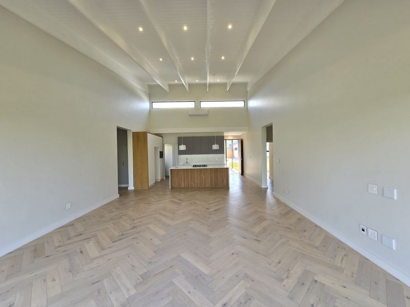 Spacious open-plan living area featuring high vaulted ceilings with exposed beams, premium herringbone timber flooring, and a modern kitchen with a central island.