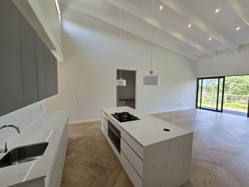 Spacious open-plan kitchen and living area featuring a large island with gas cooktop, stone countertops, herringbone timber flooring, and vaulted ceilings with exposed beams.