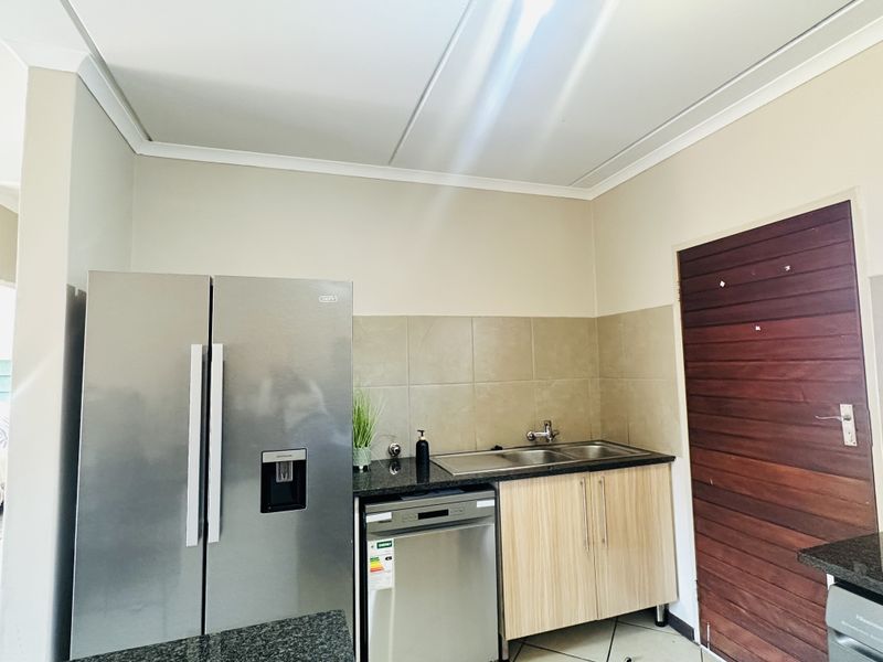 A functional scullery area featuring granite countertops, a double sink, tiled backsplash, and built-in cabinetry for additional storage and utility.