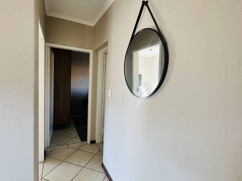 A neutral-toned hallway featuring tiled flooring and access to adjacent rooms, providing a clean and functional transition space within the home.