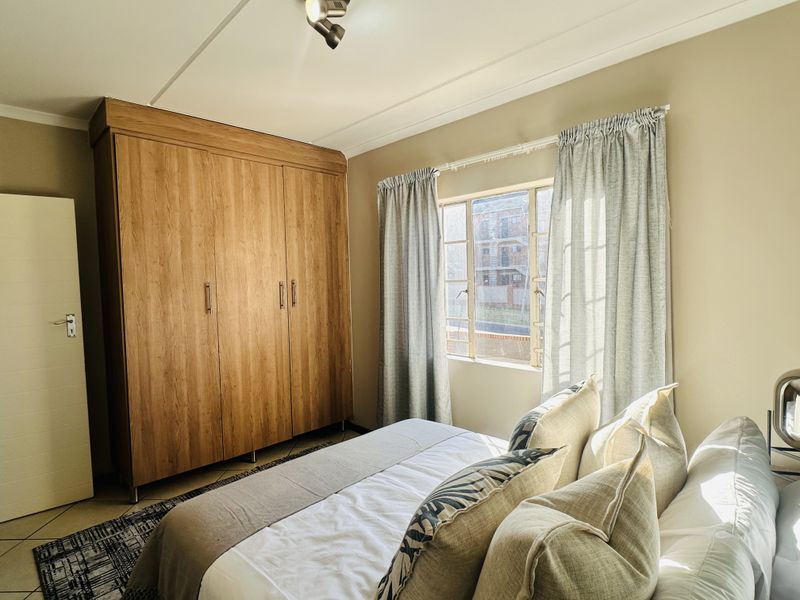 A well-lit bedroom featuring tiled flooring, a large built-in wooden wardrobe, and a window allowing natural light.
