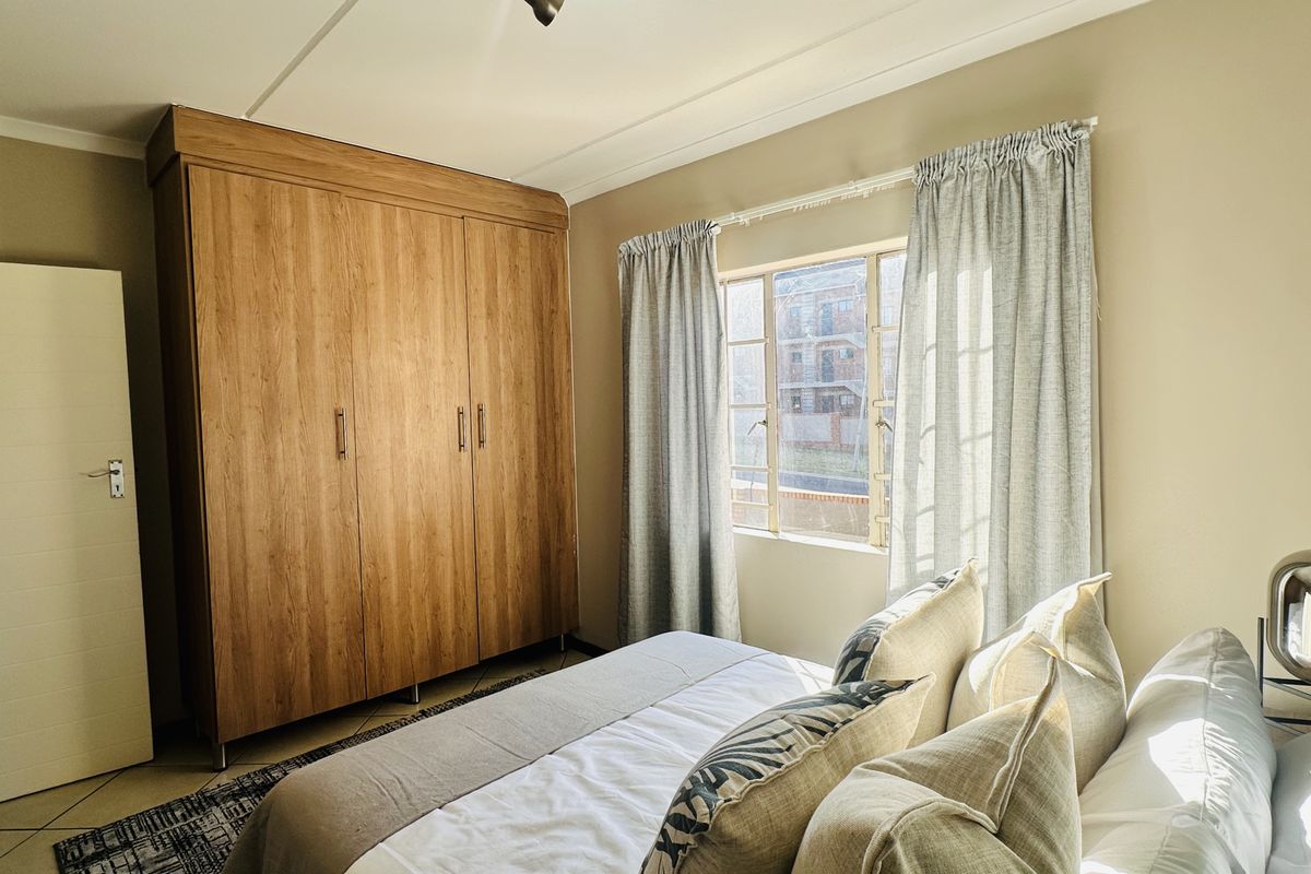 A well-lit bedroom featuring tiled flooring, a large built-in wooden wardrobe, and a window allowing natural light.