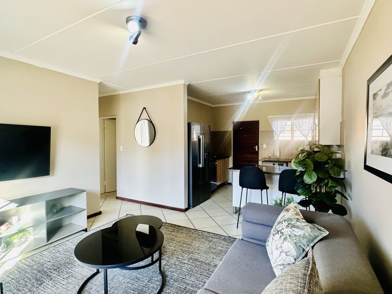 An open-plan living and kitchen area featuring tiled flooring, a breakfast bar, and functional kitchen cabinetry.
