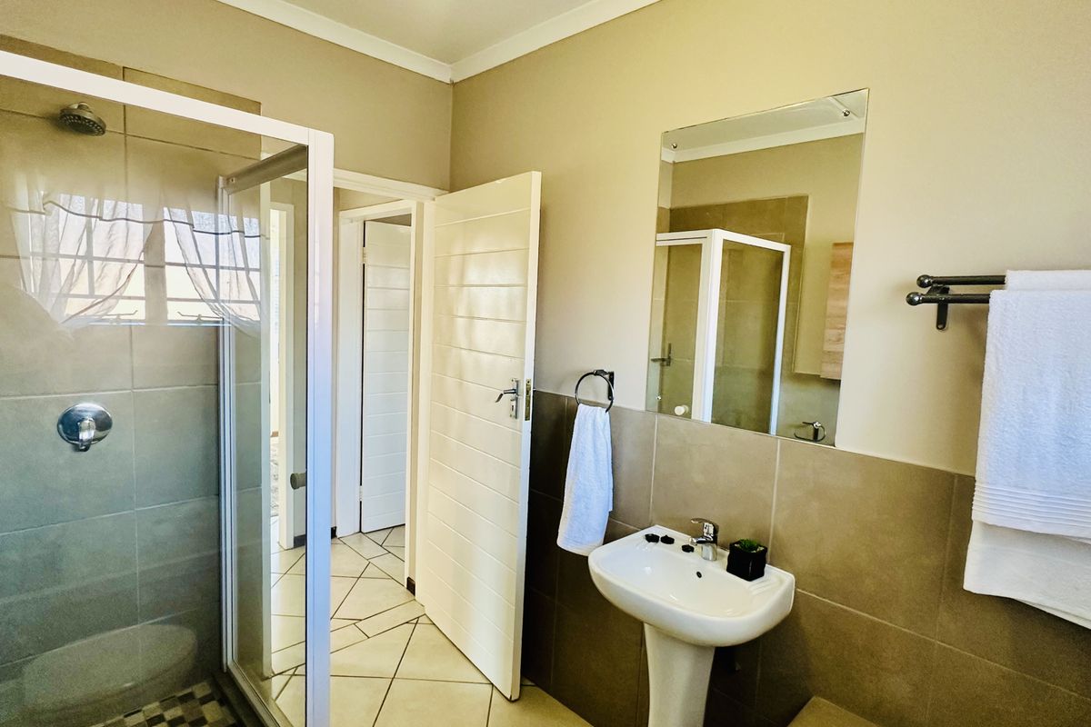 A clean and functional bathroom featuring a pedestal basin, a glass-enclosed shower, and neutral wall tiles with matching floor tiles.