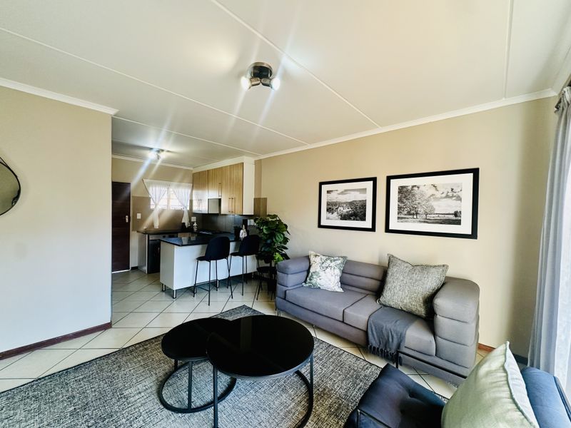An open-plan living area featuring a modern kitchen with a breakfast island, tiled flooring, and neutral wall tones, creating a functional and cohesive living space.