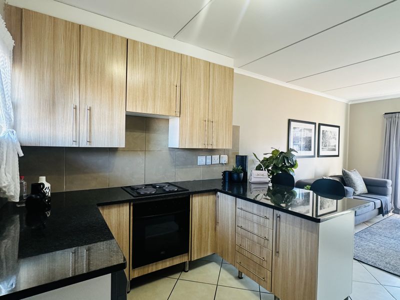 Modern open-plan kitchen featuring light wood-grain cabinetry, sleek black granite countertops, built-in oven, and hob, seamlessly flowing into the adjacent living area.