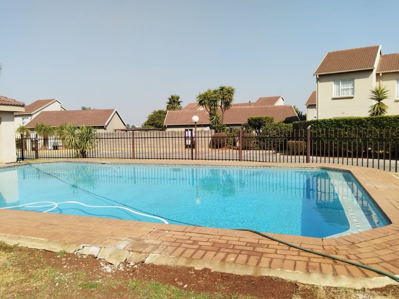 Communal swimming pool area featuring brick paving and metal perimeter fencing within a residential apartment complex.