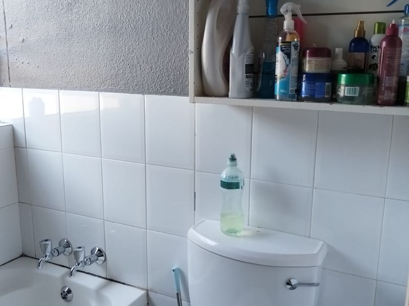 A functional bathroom featuring a standard bathtub, toilet, and wall-mounted storage shelving with tiled wall finishes.