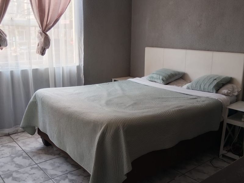 A bedroom featuring tiled flooring and a window with curtain fixtures, requiring cosmetic updates to the wall finishes.