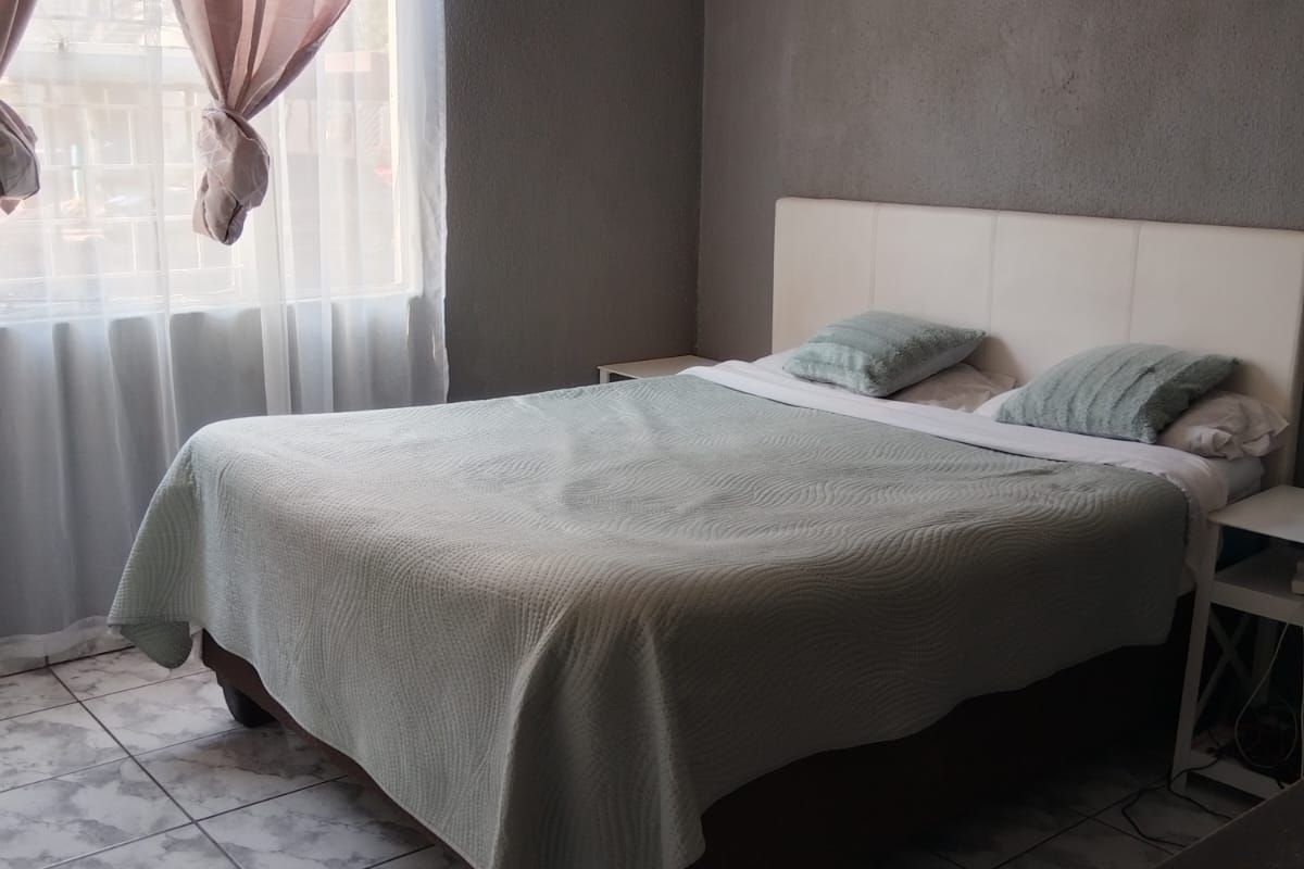 A bedroom featuring tiled flooring and a window with curtain fixtures, requiring cosmetic updates to the wall finishes.