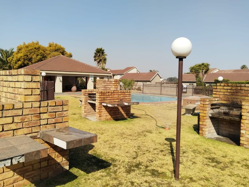 Communal pool area featuring multiple built-in brick braai stations, a swimming pool, and a covered clubhouse structure within a landscaped complex.