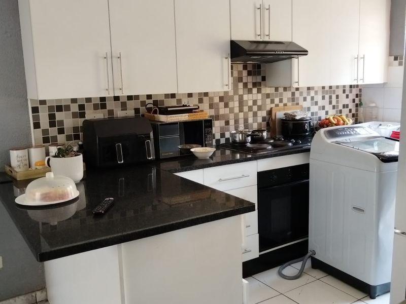 A functional kitchen featuring white cabinetry, dark granite countertops, a mosaic tile backsplash, and integrated appliances with ceramic floor tiling.