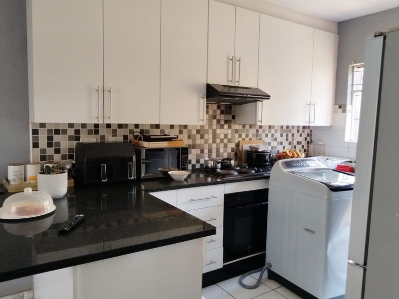 A functional kitchen featuring white cabinetry, black granite countertops, a tiled mosaic backsplash, and integrated cooking appliances.