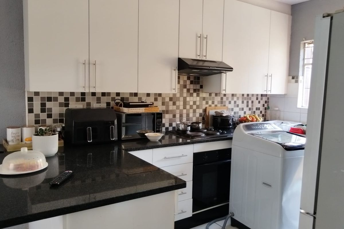 A functional kitchen featuring white cabinetry, black granite countertops, a tiled mosaic backsplash, and integrated cooking appliances.