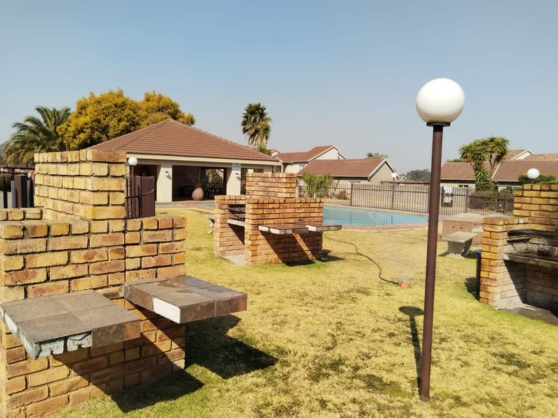 Communal outdoor area featuring multiple brick braai stands, a swimming pool, and landscaped lawn, providing a functional space for residents to enjoy.