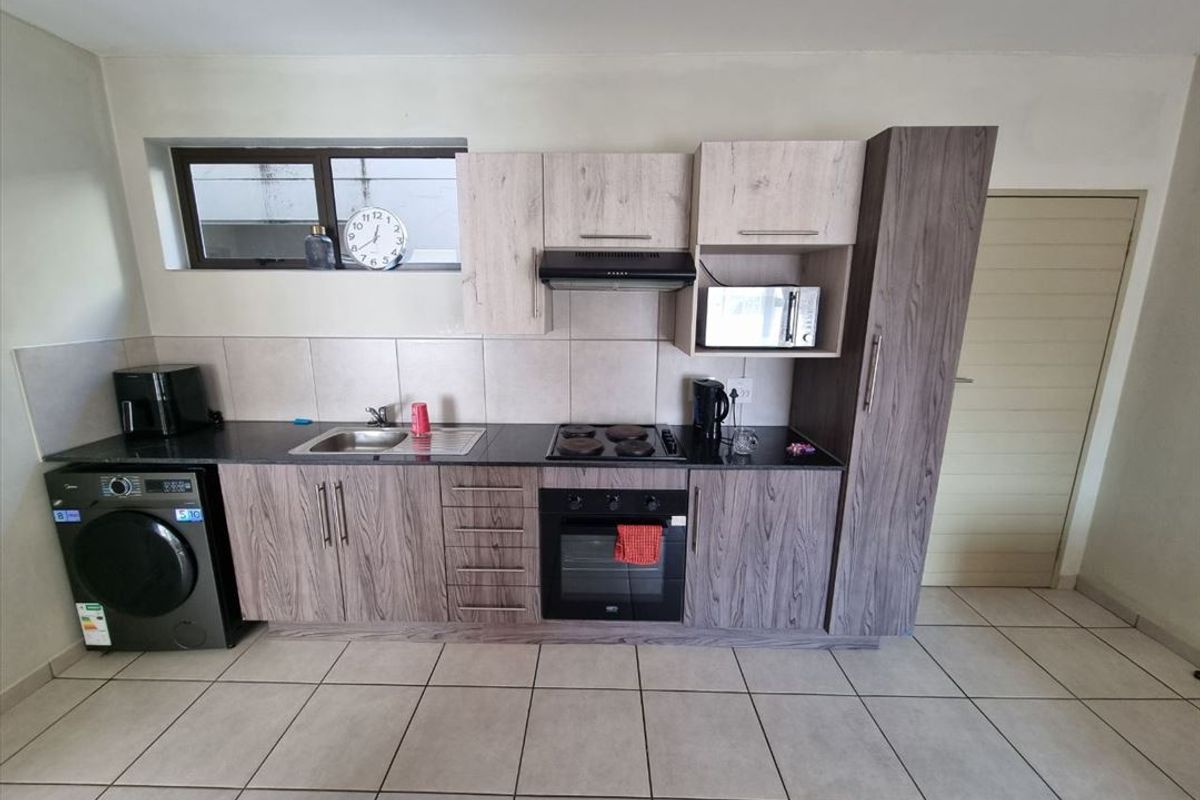 A functional kitchen featuring modern wood-grain cabinetry, dark countertops, built-in oven and hob, and tiled flooring with a neutral backsplash.