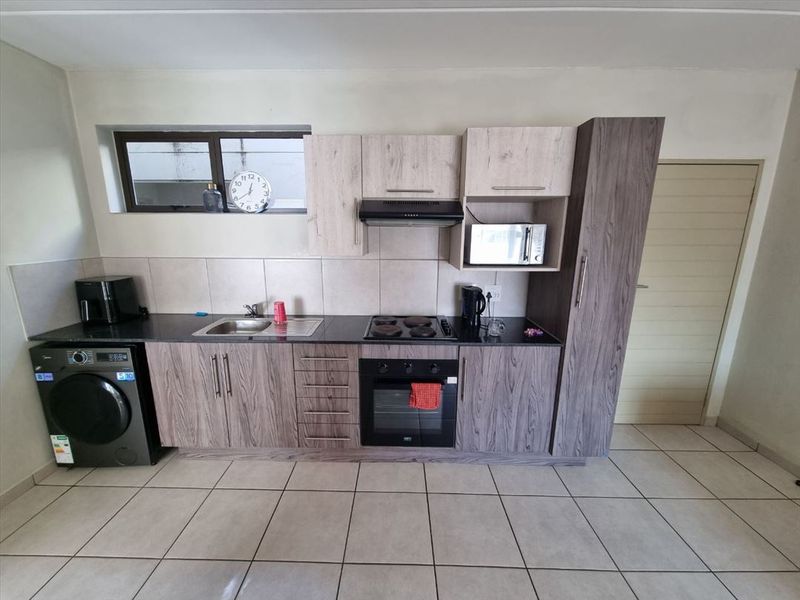 A functional kitchen featuring modern wood-grain cabinetry, dark countertops, built-in oven and hob, and tiled flooring with a neutral backsplash.