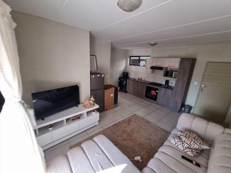 Open-plan living area featuring a functional kitchen with built-in cabinetry, oven, and hob, seamlessly connected to the lounge space with tiled flooring throughout.