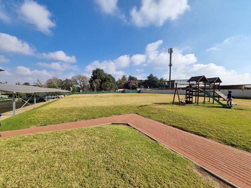 A spacious communal garden area featuring a paved walkway, a solar panel carport structure, and a children's playground set.
