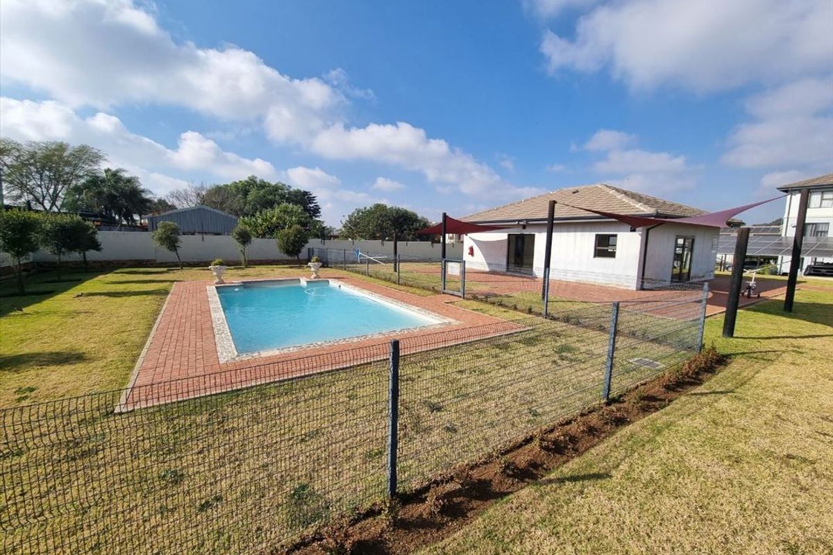 Outdoor pool area featuring a swimming pool with brick surround, shade sail, and perimeter fencing set within a landscaped garden.