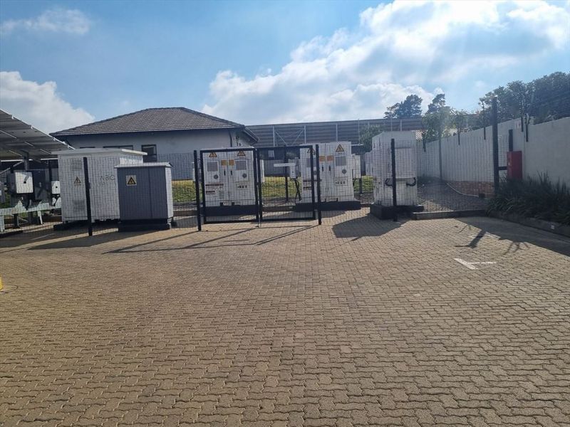 An outdoor utility area featuring paved ground, security fencing, and electrical substation infrastructure.