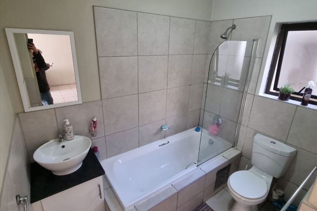 A functional bathroom featuring a tiled bathtub with a glass shower screen, a vessel sink vanity, and a standard toilet.