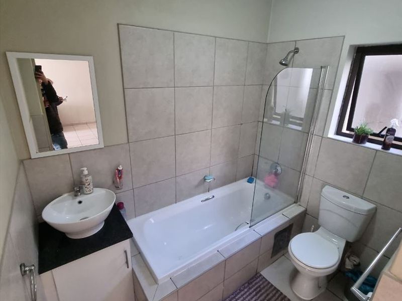 A functional bathroom featuring a tiled bathtub with a glass shower screen, a vessel sink vanity, and a standard toilet.