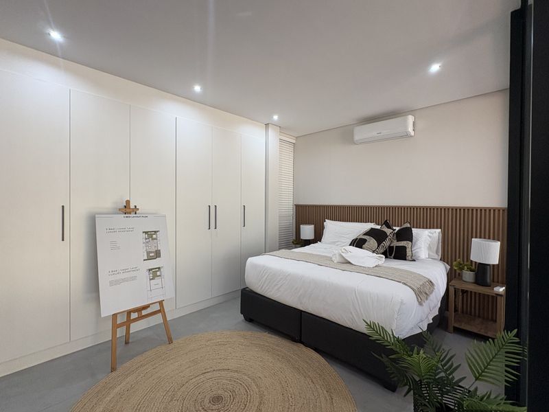 Modern bedroom featuring extensive built-in cabinetry, a timber slat headboard feature wall, split-system air conditioning, and recessed downlighting.