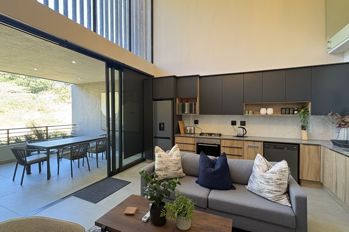 Modern open-plan living area featuring a sleek kitchen with built-in appliances, high ceilings, and seamless flow to a covered patio through large sliding doors.