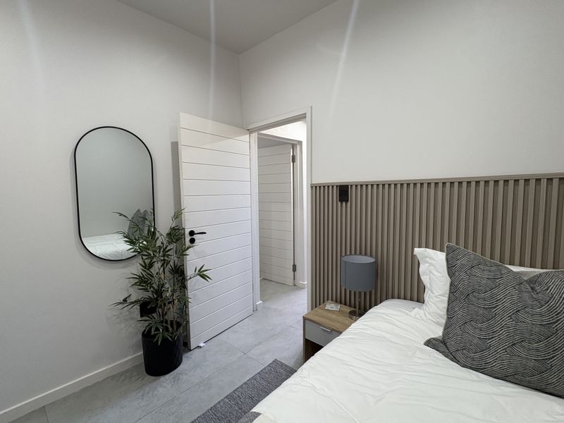 A modern bedroom featuring contemporary slatted wood wall paneling, neutral tiled flooring, and clean white interior doors.