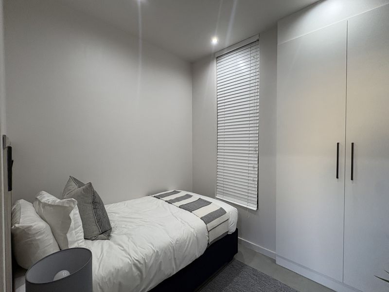 A compact, modern bedroom featuring a built-in wardrobe, venetian blinds, and recessed ceiling lighting, presented in a clean and well-maintained condition.