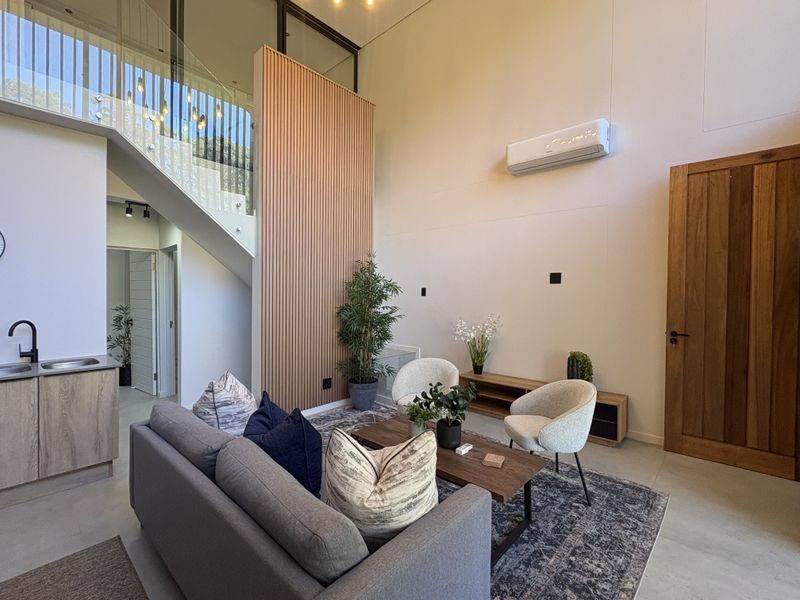 Modern open-plan living area featuring a double-volume ceiling, timber slat feature wall, glass staircase balustrade, and integrated kitchen cabinetry.