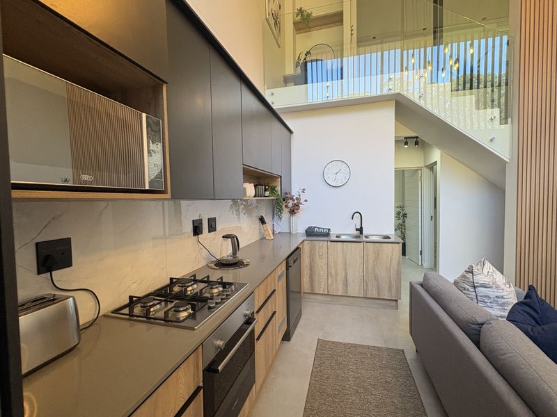 Modern open-plan kitchen featuring sleek cabinetry, stone countertops, integrated appliances, and a glass-railed staircase leading to an upper level.