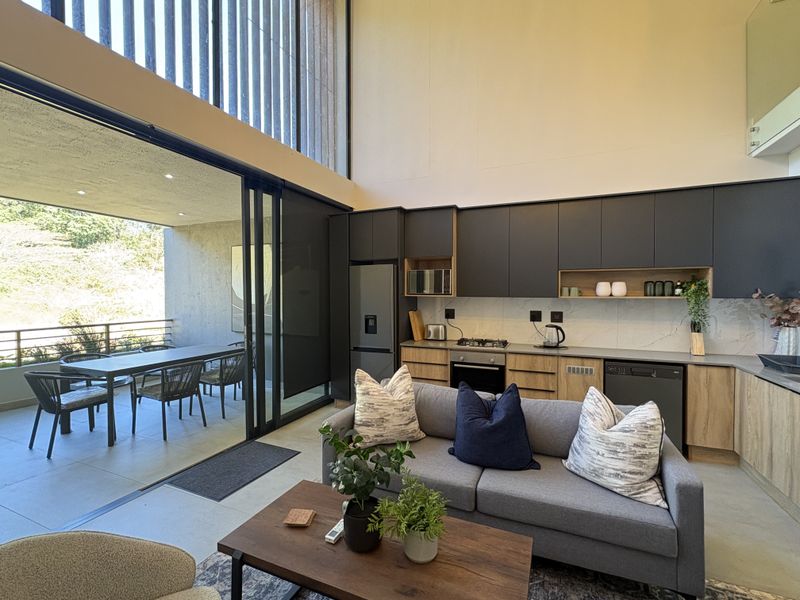 Modern open-plan living area featuring a sleek kitchen with built-in appliances, high ceilings, and seamless flow to a covered patio through large sliding doors.