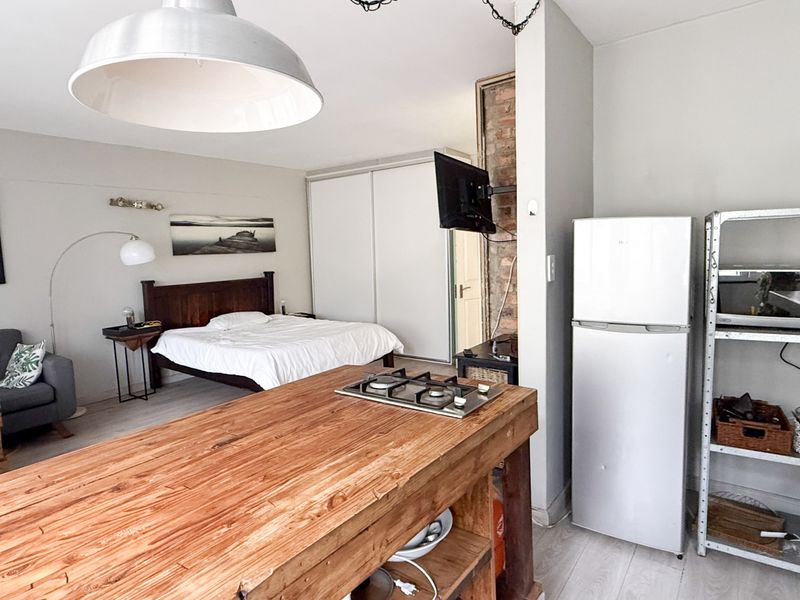Open-plan studio apartment featuring a kitchen island with gas cooktop, exposed brick detail, and built-in wardrobe storage.