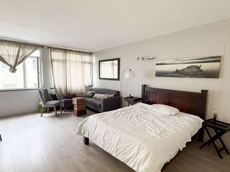 A spacious bedroom featuring light-toned laminate flooring and large windows that provide ample natural light, creating a bright and airy living environment.