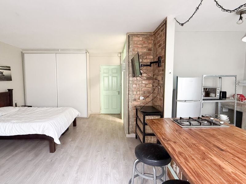 Open-plan studio apartment featuring a bedroom area with built-in storage, an exposed brick wall, and a functional kitchen with a timber breakfast bar.