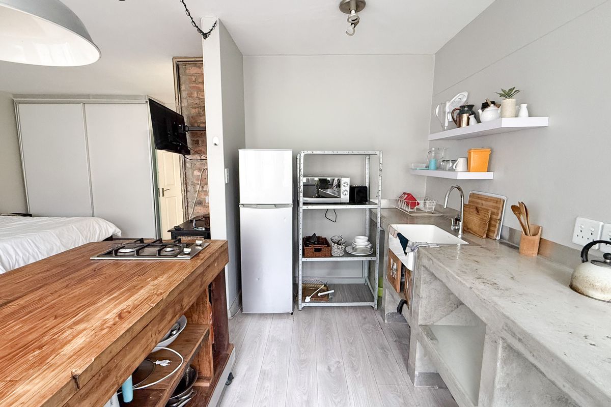 Open-plan studio apartment featuring a rustic kitchen with concrete countertops, a farmhouse sink, timber island with gas hob, and light laminate flooring.