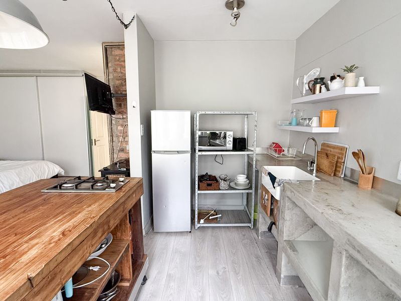 Open-plan studio apartment featuring a rustic kitchen with concrete countertops, a farmhouse sink, timber island with gas hob, and light laminate flooring.