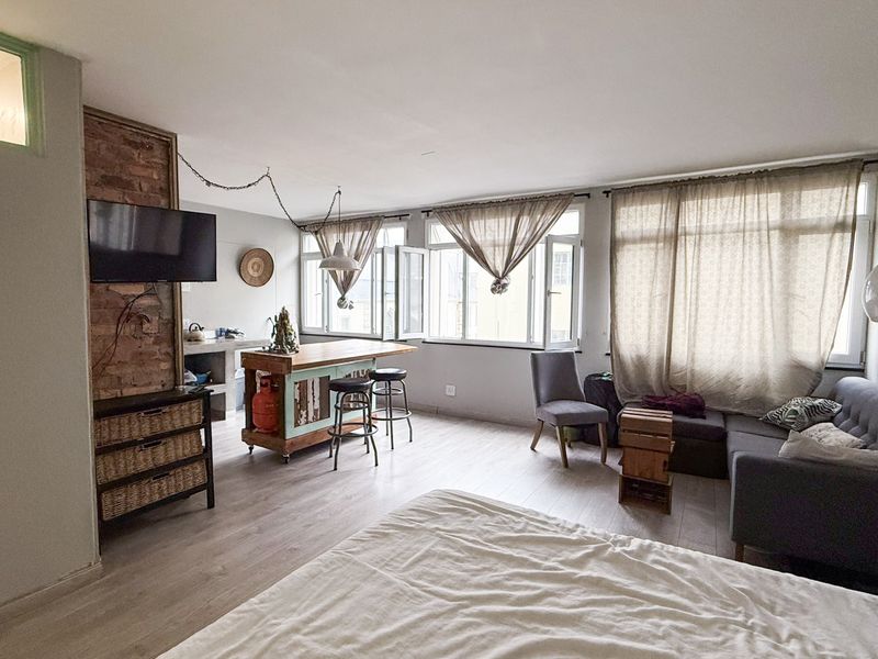 Open-plan living area featuring laminate flooring, an exposed brick accent wall, and large windows providing natural light.