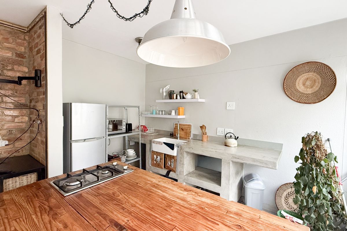 A rustic-style kitchen featuring an exposed brick wall, concrete countertops, a farmhouse sink, and a wooden island with an integrated gas hob.