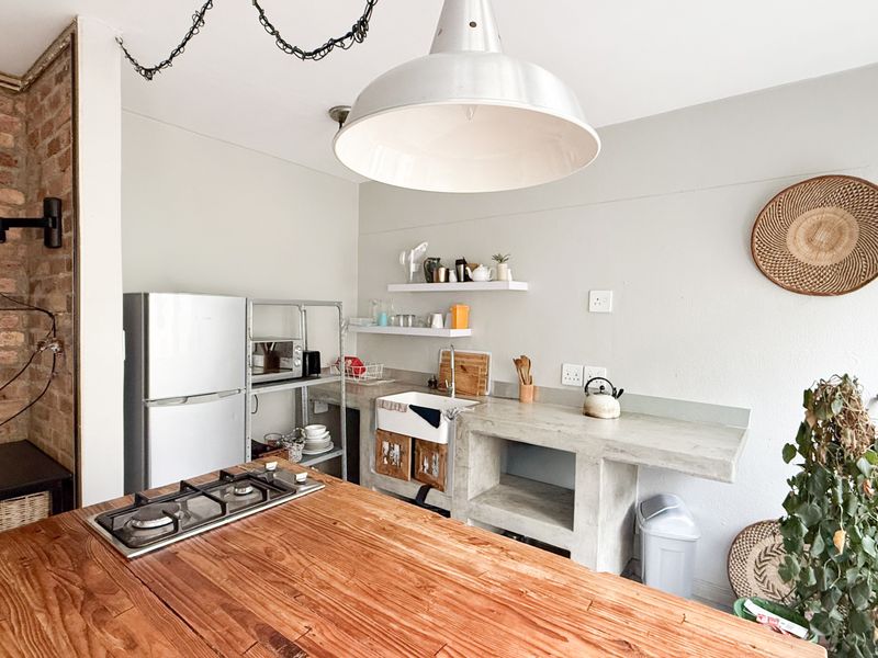 A rustic-style kitchen featuring an exposed brick wall, concrete countertops, a farmhouse sink, and a wooden island with an integrated gas hob.