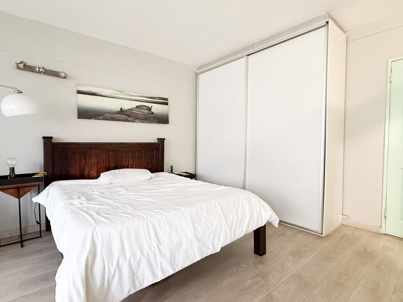 A well-lit bedroom featuring light-toned laminate flooring and a large built-in wardrobe with sliding doors.