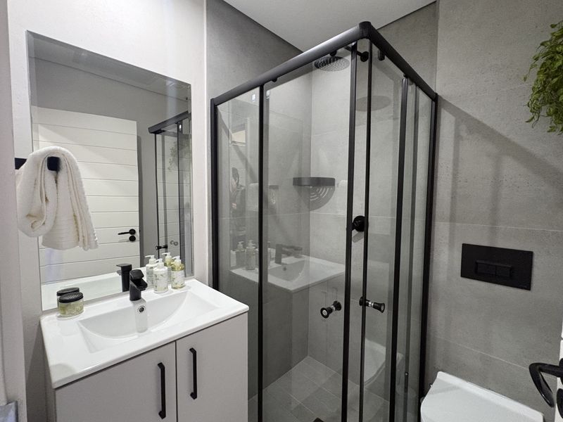 Modern bathroom featuring a sleek vanity with basin, a glass-enclosed shower with black fixtures, and contemporary grey wall tiling.
