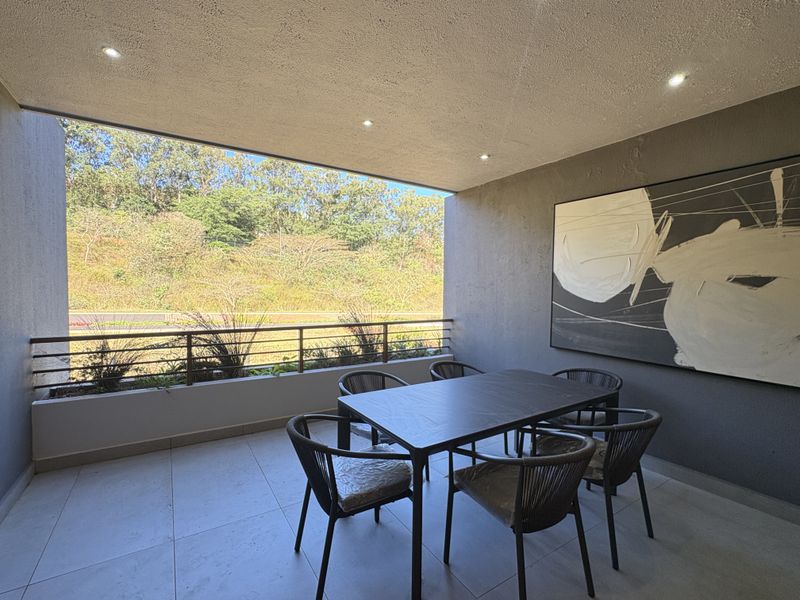 A covered balcony featuring tiled flooring, recessed downlighting, and a metal balustrade, offering an open view of the surrounding landscape.